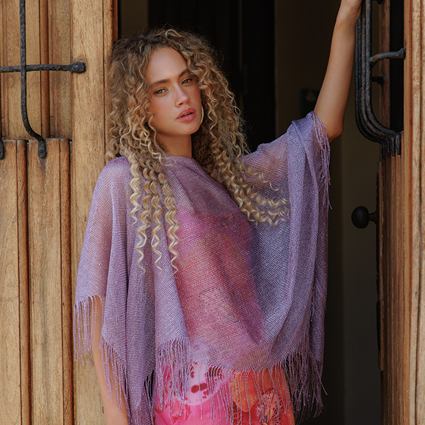 Person standing in a doorway wearing a lavender fringed shawl over a colorful outfit.