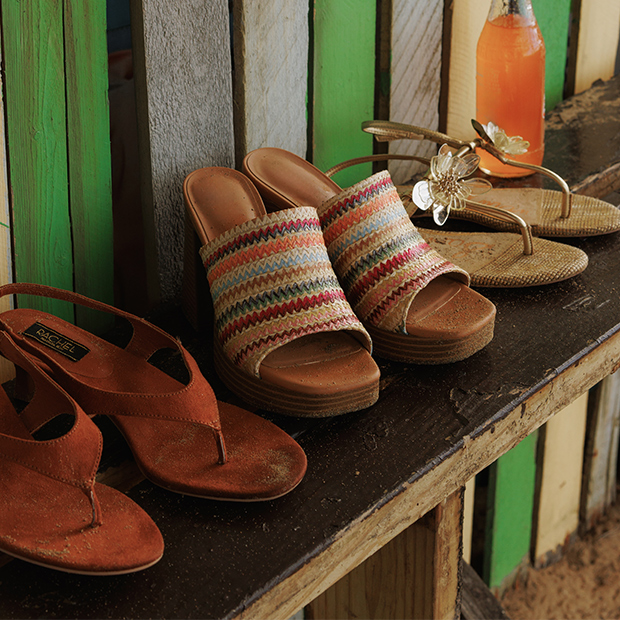 Colorful woven slide sandals and brown sandals displayed on a rustic wooden bench.